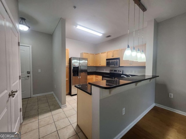 kitchen with kitchen peninsula, appliances with stainless steel finishes, light brown cabinetry, light tile patterned floors, and decorative light fixtures