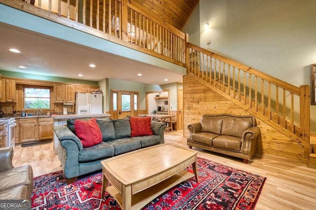 living room with wood walls, light hardwood / wood-style floors, sink, and high vaulted ceiling