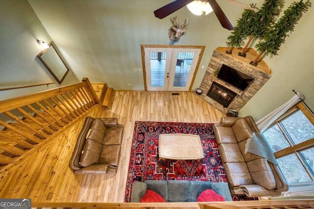 living room with a stone fireplace, hardwood / wood-style floors, ceiling fan, and french doors