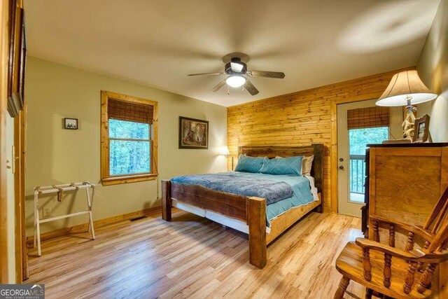 bedroom with multiple windows, wooden walls, light wood-type flooring, and ceiling fan