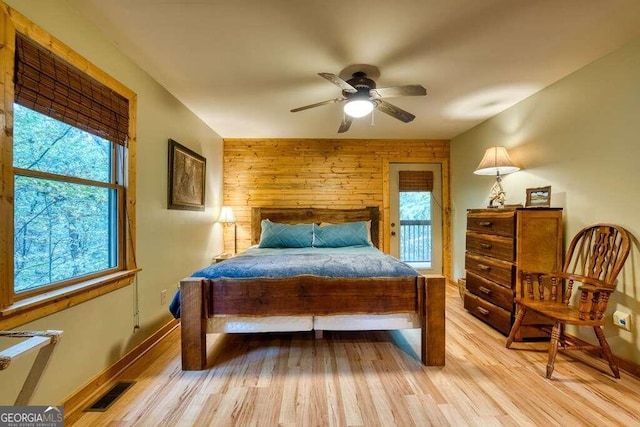 bedroom with light hardwood / wood-style floors, multiple windows, wooden walls, and ceiling fan