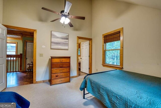 bedroom with a high ceiling, light carpet, multiple windows, and ceiling fan