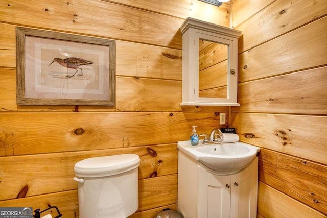 bathroom with toilet, vanity, and wooden walls