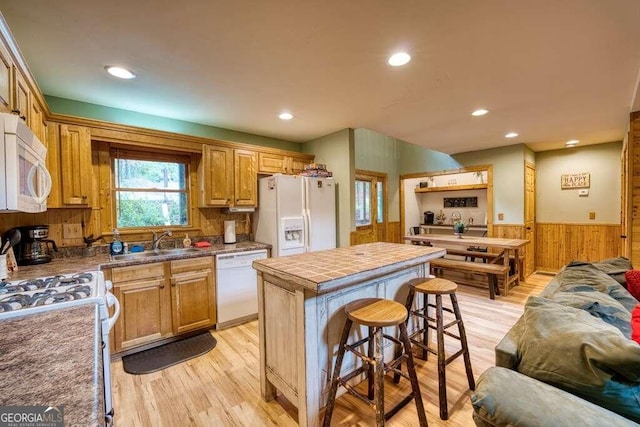 kitchen featuring tile counters, a kitchen island, a breakfast bar, light wood-type flooring, and white appliances