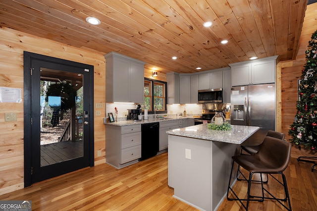 kitchen with wood walls, a center island, light hardwood / wood-style flooring, light stone countertops, and stainless steel appliances