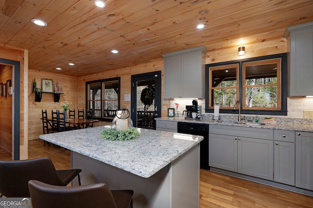 kitchen with sink, wood walls, light hardwood / wood-style floors, gray cabinets, and a kitchen island