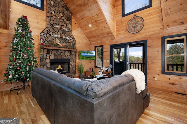 living room with a stone fireplace, high vaulted ceiling, wooden walls, wood ceiling, and light wood-type flooring