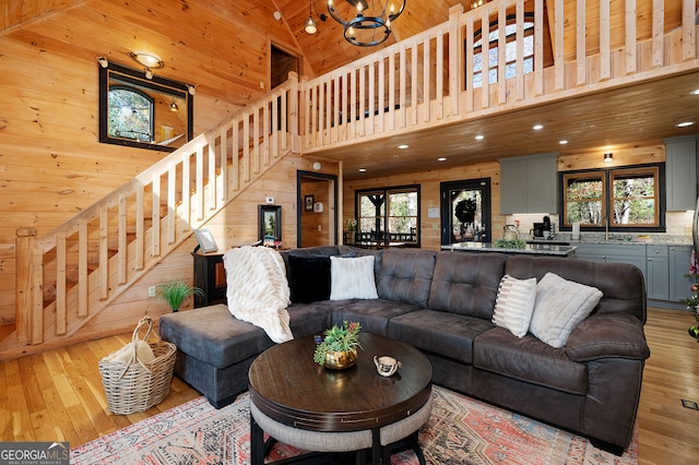 living room featuring a towering ceiling, light hardwood / wood-style floors, a healthy amount of sunlight, and wood walls