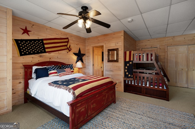 carpeted bedroom with wood walls, a drop ceiling, and ceiling fan