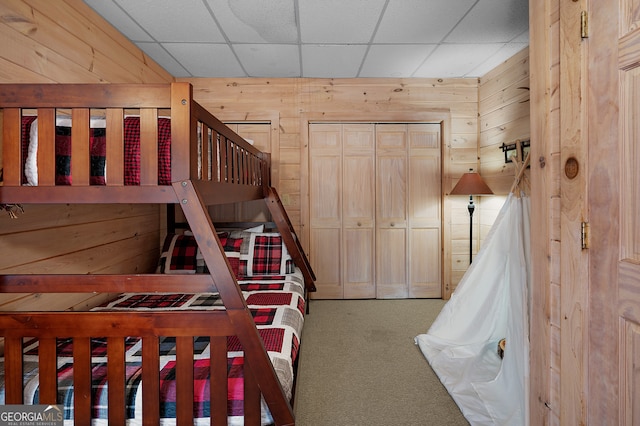 bedroom featuring carpet flooring, a drop ceiling, and wooden walls