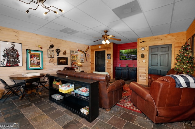 living room featuring a drop ceiling, wood walls, and ceiling fan