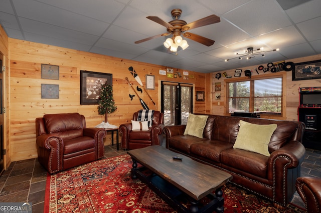 tiled living room with wood walls, a drop ceiling, and ceiling fan