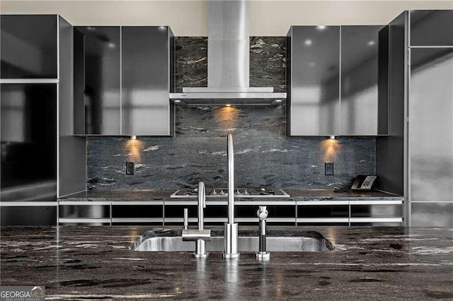 kitchen with tasteful backsplash, dark stone counters, stainless steel gas cooktop, sink, and wall chimney range hood