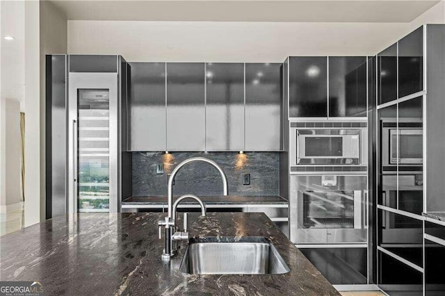 kitchen featuring sink, beverage cooler, oven, dark stone counters, and decorative backsplash