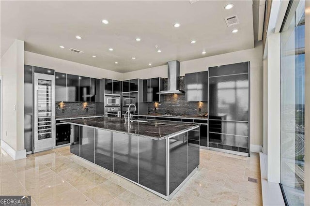 kitchen featuring decorative backsplash, a spacious island, wall chimney range hood, and appliances with stainless steel finishes