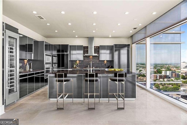 kitchen with a large island, wall chimney exhaust hood, backsplash, and a breakfast bar area