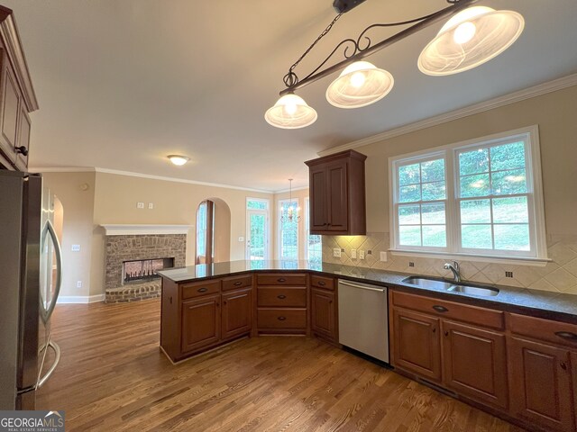 kitchen with sink, kitchen peninsula, pendant lighting, a fireplace, and appliances with stainless steel finishes