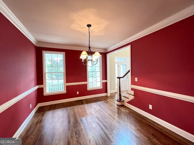 unfurnished dining area with dark wood-type flooring, crown molding, and an inviting chandelier