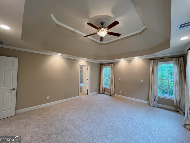 empty room with a raised ceiling, crown molding, ceiling fan, and light carpet