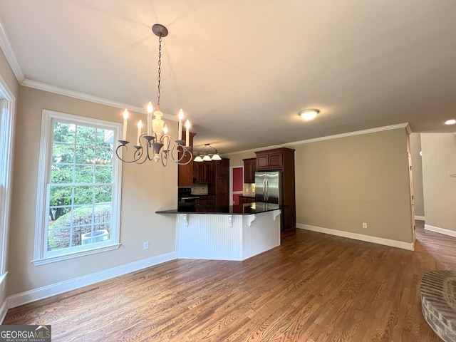 kitchen with dark wood-type flooring, a notable chandelier, kitchen peninsula, crown molding, and a breakfast bar