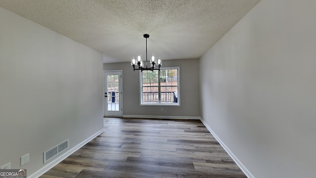 unfurnished dining area featuring dark wood-type flooring, a chandelier, and a textured ceiling