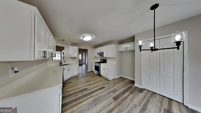 kitchen featuring white cabinets, stainless steel appliances, decorative light fixtures, and light hardwood / wood-style flooring