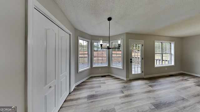 unfurnished dining area with a textured ceiling, an inviting chandelier, a healthy amount of sunlight, and light hardwood / wood-style flooring