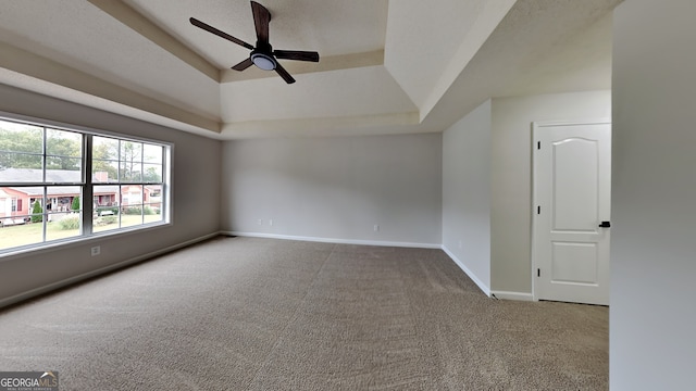 carpeted empty room featuring ceiling fan and a raised ceiling