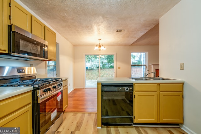 kitchen with sink, stainless steel appliances, an inviting chandelier, a textured ceiling, and light wood-type flooring