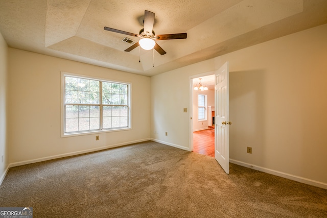 spare room with a raised ceiling, ceiling fan with notable chandelier, carpet floors, and a textured ceiling