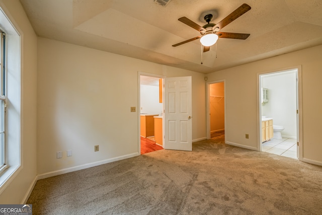 unfurnished bedroom with light carpet, a walk in closet, ceiling fan, connected bathroom, and a closet