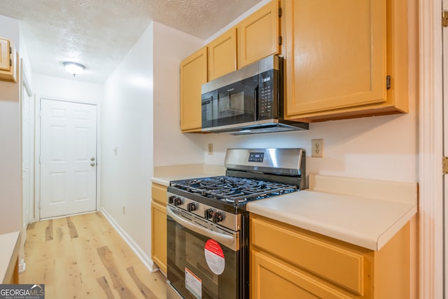 kitchen featuring light brown cabinets, a textured ceiling, stainless steel appliances, and light hardwood / wood-style flooring