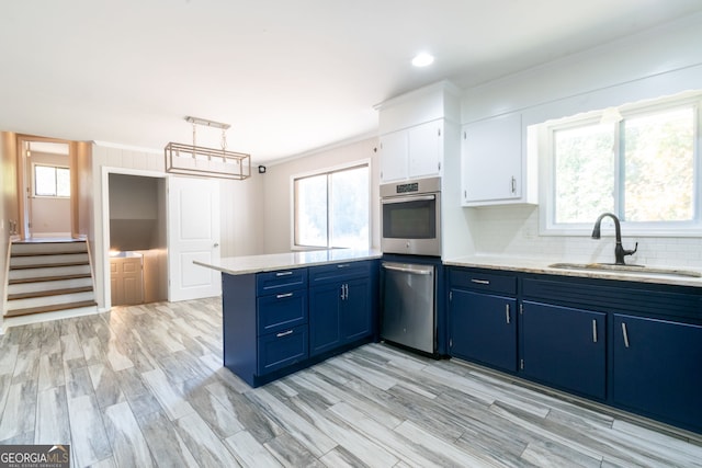 kitchen with sink, appliances with stainless steel finishes, a healthy amount of sunlight, white cabinets, and pendant lighting