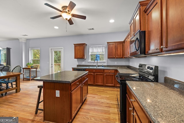 kitchen featuring light wood-type flooring, a breakfast bar area, black appliances, and a kitchen island