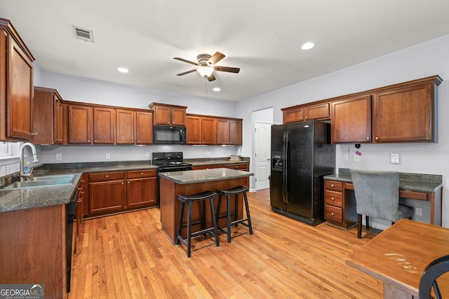 kitchen with built in desk, sink, black appliances, a kitchen island, and light wood-type flooring