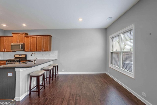 kitchen featuring stainless steel appliances, sink, a kitchen bar, dark hardwood / wood-style flooring, and decorative backsplash