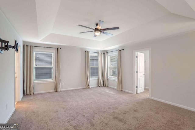 spare room featuring ceiling fan, light colored carpet, and a raised ceiling