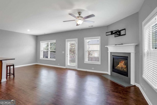 unfurnished living room featuring dark wood-type flooring, a wealth of natural light, and ceiling fan