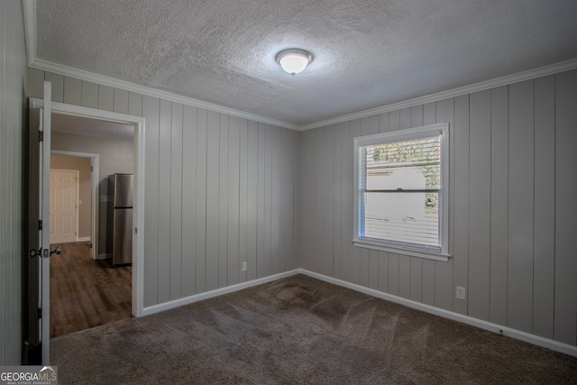 carpeted spare room featuring wood walls, a textured ceiling, and crown molding