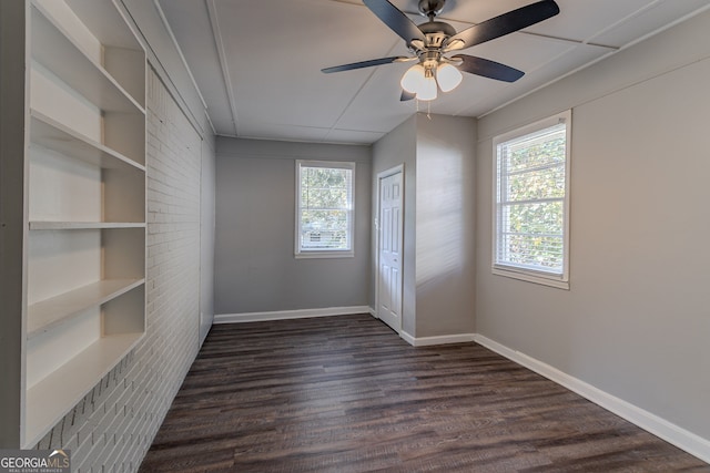 unfurnished room with plenty of natural light, dark wood-type flooring, ceiling fan, and brick wall