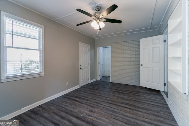 unfurnished room featuring brick wall, dark hardwood / wood-style floors, and ceiling fan