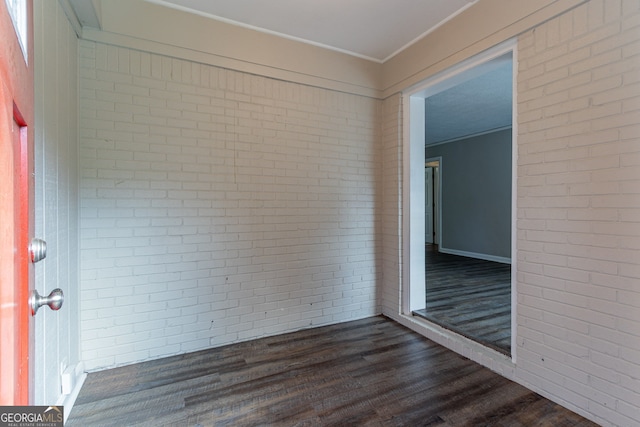 spare room featuring dark hardwood / wood-style flooring and brick wall