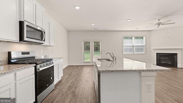 kitchen with sink, appliances with stainless steel finishes, light stone countertops, an island with sink, and white cabinets