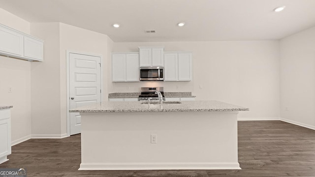 kitchen with white cabinetry, appliances with stainless steel finishes, a kitchen island with sink, and light stone counters