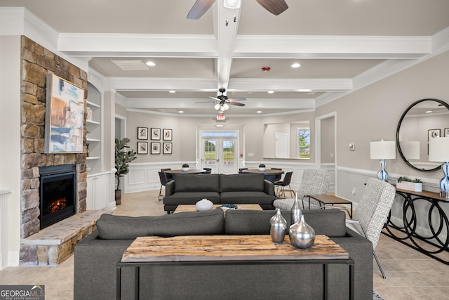 living room featuring beam ceiling, ornamental molding, built in shelves, a stone fireplace, and french doors