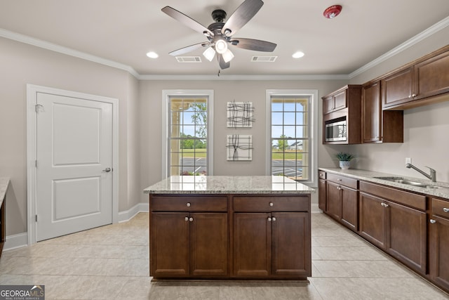 kitchen with sink, dark brown cabinets, stainless steel microwave, light stone counters, and ornamental molding