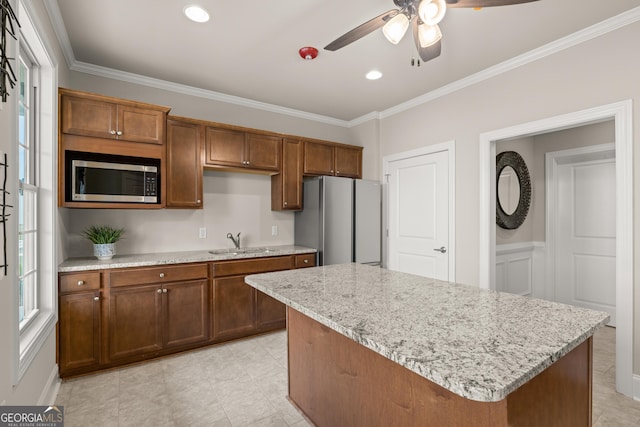 kitchen with a kitchen island, appliances with stainless steel finishes, sink, ornamental molding, and light stone countertops