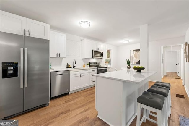 kitchen with white cabinetry, a kitchen bar, appliances with stainless steel finishes, light hardwood / wood-style floors, and backsplash