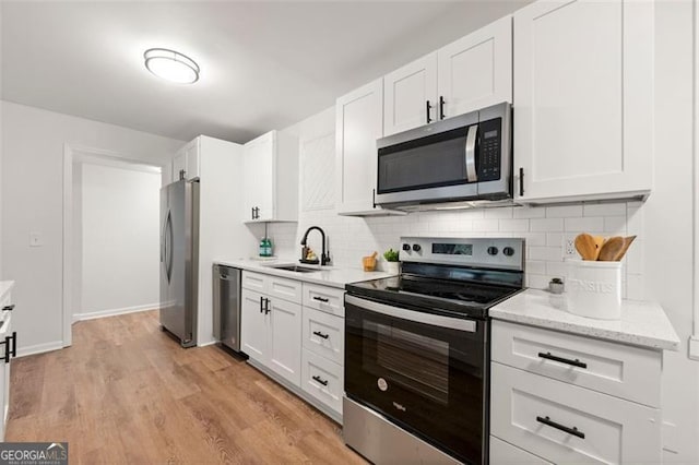 kitchen featuring white cabinets, sink, backsplash, light wood-type flooring, and stainless steel appliances