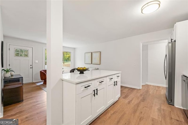 kitchen featuring white cabinets, light wood-type flooring, stainless steel refrigerator, and light stone counters